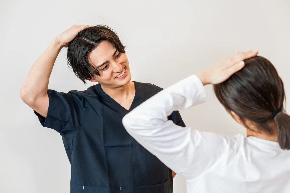 施術者が腕を上げる動きで肩・腕の可動域を確認している様子